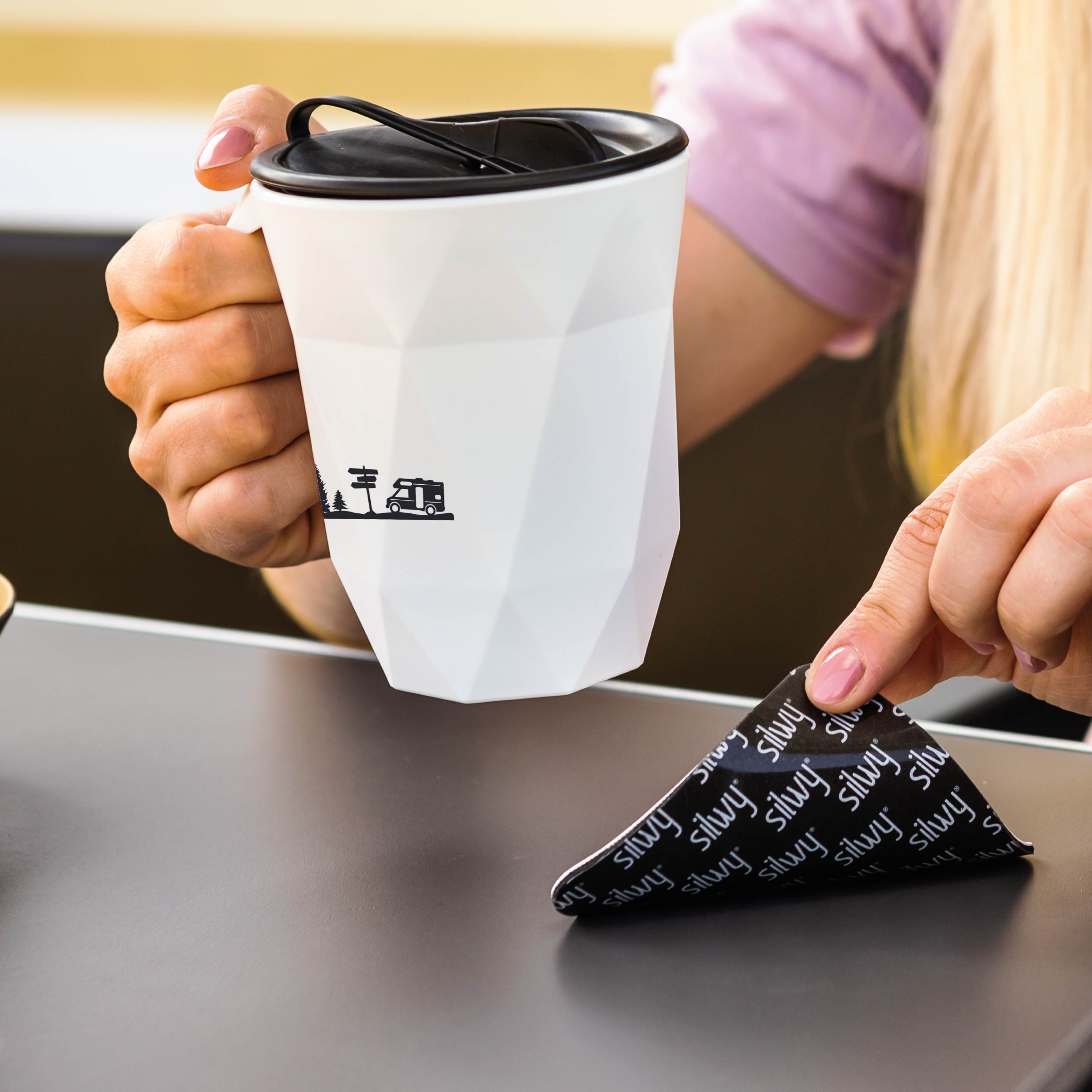 Magnet-Kunststofftasse TO-GO mit Camper-Motiv in der Luft und zugehörigem quadratischem Metall-Nano-Gel-Pad auf Tisch